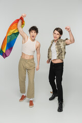excited pangender partners with lgbt flag gesturing with clenched fists and screaming on grey...