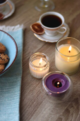 Plate of chocolate pralines, bowl of cookies, cups of tea, glasses of juice and lit candles on the table. Selective focus.