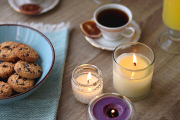 Plate of chocolate pralines, bowl of cookies, cups of tea, glasses of juice and lit candles on the table. Selective focus.