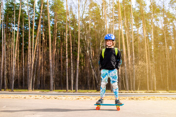 happy child schoolboy with a backpack goes to school on a skateboard. a joyful boy with protection on his knees and elbows, with a helmet on his head, stands on a plastic bright city cruiser skateboar