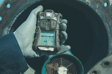 Worker hand holding gas detector inspection safety gas testing at front manhole tank