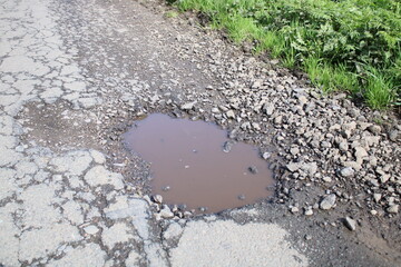 Large pothole on the side of a country road filled with water