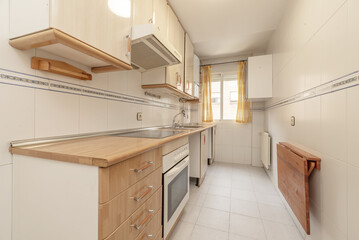 Small kitchen furnished without washing machine or dishwasher with wooden folding table and window with yellow curtains