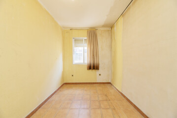 Obraz premium A room in a shabby apartment in need of a good coat of paint on the walls and a window with old curtains with brown tiled floors