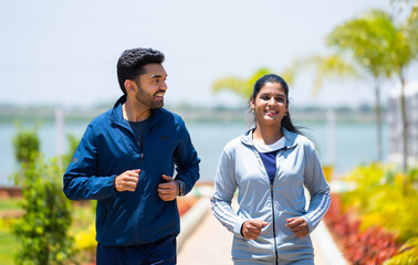 Happy Young couple jogging in park while talking each other during morning - concept of fitness,...