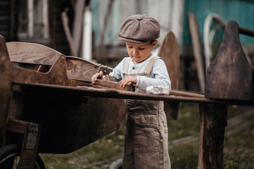 A young boy aviator in a homemade airplane in a natural landscape with a machine tool in his hands repairs a wing. The authentic mood of the picture. Vintage.