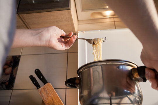 Hot instant pasta is cooked in a saucepan on the stove in the kitchen. The girl stirs the food in the bowl with a fork. Image for your creative decoration and design.