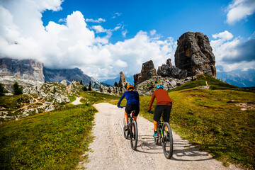 A man and woman ride electric mountain bikes in the Dolomites in Italy. Mountain biking adventure on beautiful mountain trails. - 589891166