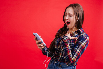 Naklejka premium Laughing girl looking at the screen of the phone while standing on a red background