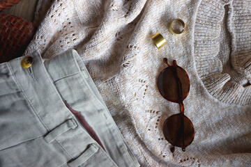 Vintage sweater, neutral trousers, wicker bag, leopard scarf, brown shoes, sunglasses and brass rings on wooden background. Top view.