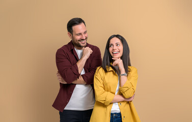 Romantic young man looking at beautiful girlfriend smiling with hand on chin. Happy attractive couple dressed in casuals posing cheerfully while standing against beige background