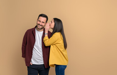 Side view of young woman covering ear of handsome smiling boyfriend while telling him gossip on...