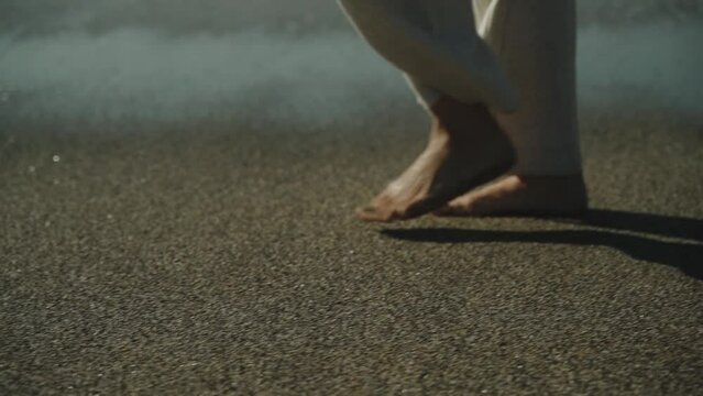 Slender woman's legs walking along the sandy beach. White developing pants