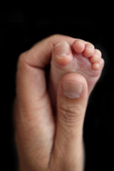 Mother is doing massage on her baby foot. Close up baby feet in mother hands on a black background. Prevention of flat feet, development, muscle tone, dysplasia. Family, love, care, and health concept