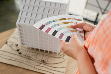 partial view of designer holding color palette near house model in office.