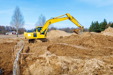 Obraz premium Excavator dig the trenches at a construction site. Trench for laying external sewer pipes. Sewage drainage system for a multi-story building. Digging the pit foundation