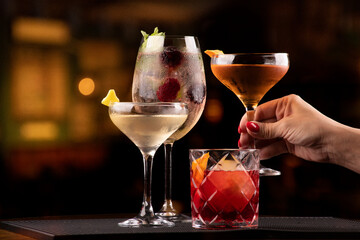 cocktail collection with vesper negroni weesky and lillet with berries and mint in bar rubber holder with blurred pub background and female hand picking one of them landscape