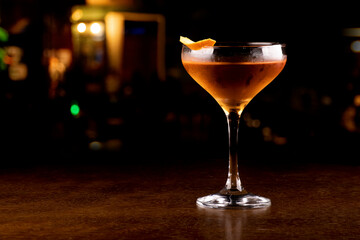 Cocktail glass with whiskey and orange peel garnish close-up on blurred pub background