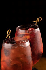 macro closeup on two cocktail glasses with rosato rose wine and berries as garnish and ice isolated on wooden table and black background