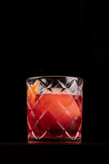 negroni cocktail seen from above with round orange ice on wooden table from the front with isolated black background