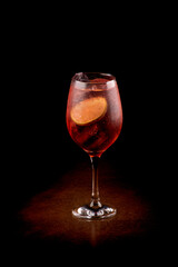 refreshing glass of lillet spritz aperol cocktail with lime and ice on wooden table with dark background seen at angle