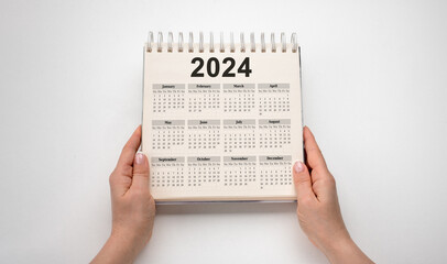Fototapeta na wymiar Hands hold Calendar Year 2024 schedule. 2024 desk calender notepad on wooden table and gray background. New Year. plans for 2024. white background