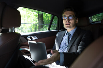 Depressed businessman sitting on backseat of his luxury car and feeling bad after overloaded work day in the office