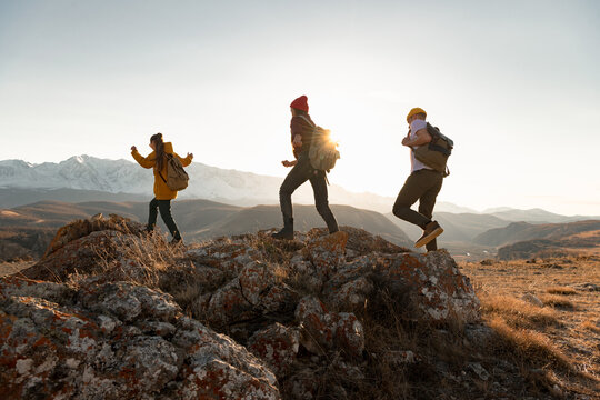 Group of young hikers walks in mountains at sunset. Silhouettes of walking tourists with backpacks