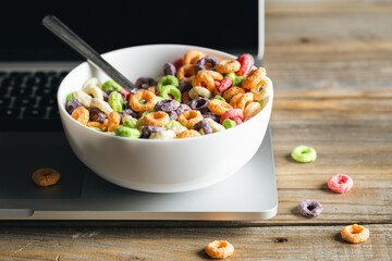 Colored breakfast cereals in a bowl and laptop, workplace breakfast, quick healthy breakfast in the office in the morning.