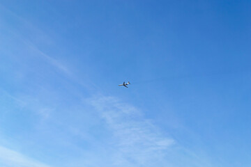 The plane flies high in the blue sky with small clouds