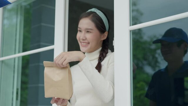 Happy smiling Asian woman receives paper bag parcel of food from courier front house. Delivery man send deliver express. online shopping, paper container, takeaway, postman, delivery service, packages