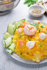 Omelet and shrimp on rice with cucumber in gray dish on concrete table. (Scrambled egg)