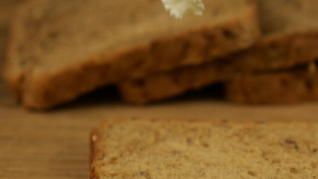 Cream cheese spread with a knife on a piece of multigrain bread on a wooden cutting board.