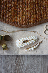 Vintage neutral bag, pearl hair barrettes, gold necklace, earrings and brass rings on wooden background. Top view.