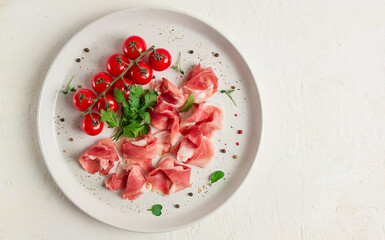 sliced prosciutto, appetizer, with cherry tomatoes, on a white plate, top view,