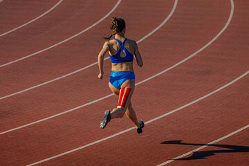 female runner running on red track stadium, kinesiotaping on back thigh, typical injury for...