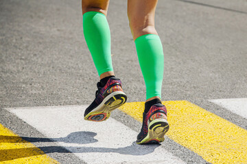 Fototapeta na wymiar legs female runner in bright green compression socks running pedestrian crossing on road
