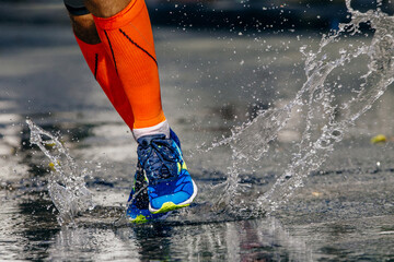 close-up legs male runner in compression socks running puddle on road, splashes and drops from under your feet