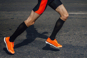 legs male runner in black compression socks and bright running shoes, shadow man jogger in dark asphalt