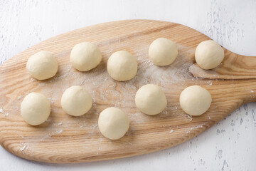 Fototapeta na wymiar Wooden board with raw dough balls for homemade buns on a light gray background, top view. Baking homemade buns