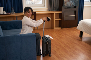 Joyous woman with travel documents and luggage in luxury suite