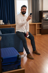 Joyous tourist using his smartphone in hotel room