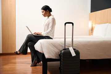 Concentrated young female working on laptop in hotel room