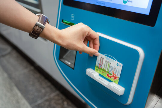 SINGAPORE - APR 19, 2022: Lady's hand placing the Singapore MRT Card (EZ-Link) at the card reader area of the ticket machine. Passenger reload EZ-Link Card using Ticket vending machine.