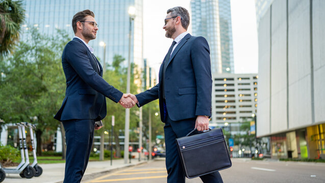 Business man shaking hands. Two businessmen handshake outdoor. Handshake business people. Handshake of two business man outdoor. Business man wearing modern suit in building city background.