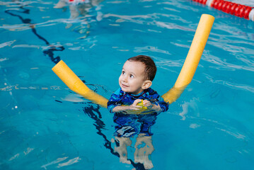 Happy little boy learning to swim with pool noodle