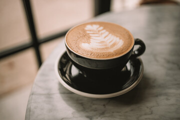 Black cup of cappuccino with latte art on white background. Beautiful foam, greenery ceramic cups, stylish toning, place for text. High quality photo