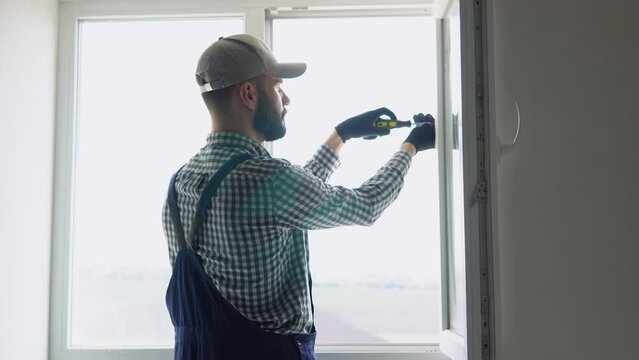 Man in uniform does pvc window installation with a screwdriver