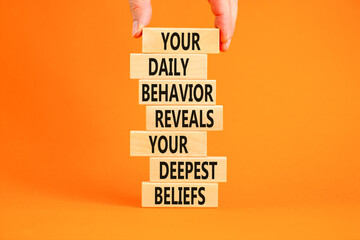 Behavior symbol. Concept words Your daily behavior reveals your deepest beliefs on wooden blocks. Beautiful orange background. Copy space. Businessman hand. Motivational business behavior concept.