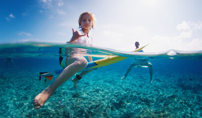 Boy surfs with his father. Preteen boy sits on the surf board in the tropical ocean with his family